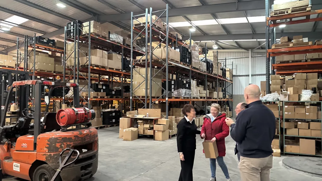 IMG_3297 Showing a warehouse with boxes on shelves and people talking.