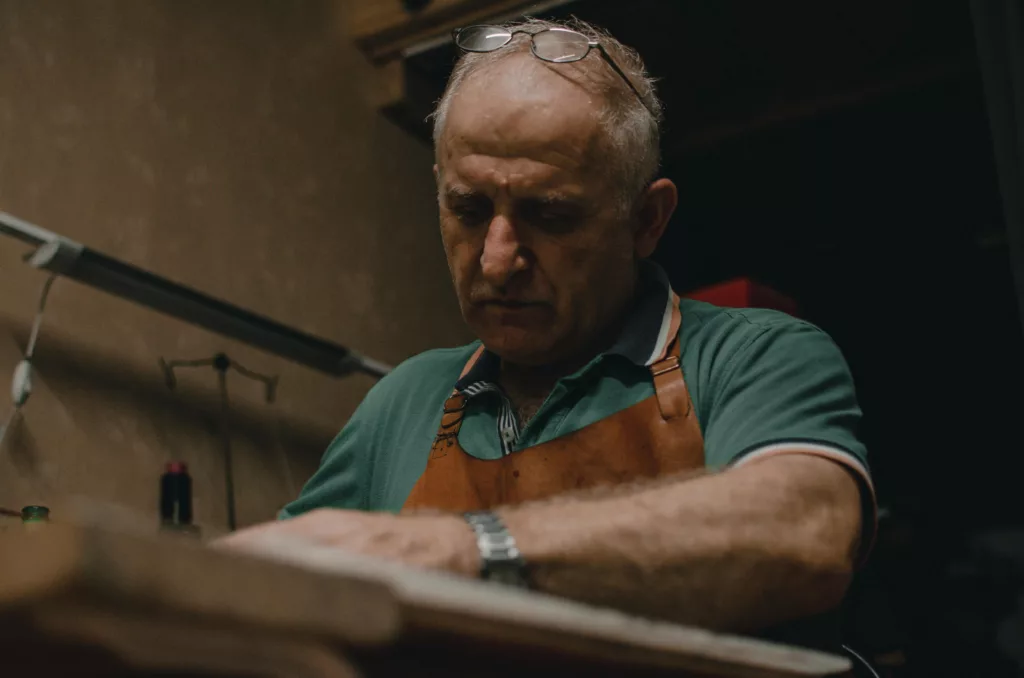 Senior artisan in eyeglasses crafting indoors with focus and skill, wearing apron.